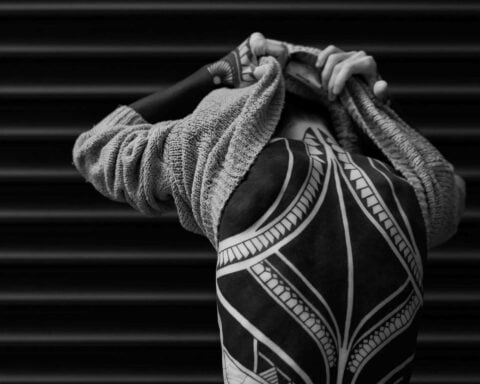 Man with a full back tribal style tattoo taking off his sweater.