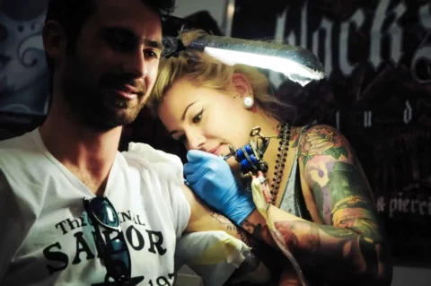 Female tattoo artist tattooing the shoulder of a man